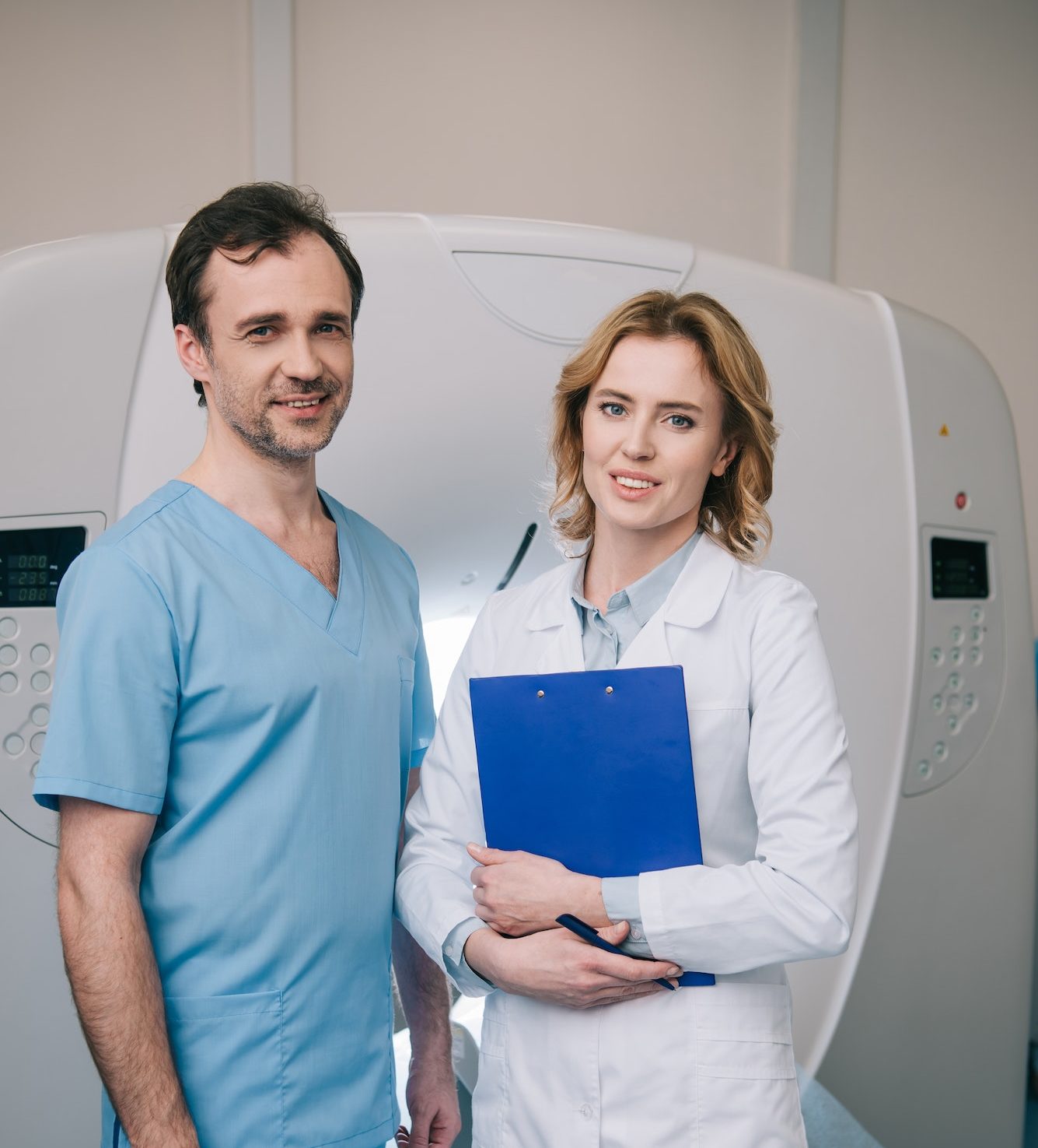 beautiful-radiologist-holding-clipboard-while-standing-near-assistant-and-looking-at-camera-e1682350841592.jpg